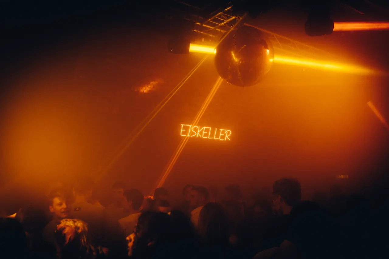 Clubnacht mit Gästen, Lichtstrahlen und Discokugel im Eiskeller