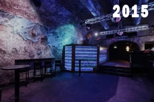 Innenansicht des Eiskeller Clubs im Jahr 2015 mit blau-violetter Beleuchtung, Lichttraversen und einem Tresen aus Glaselementen.